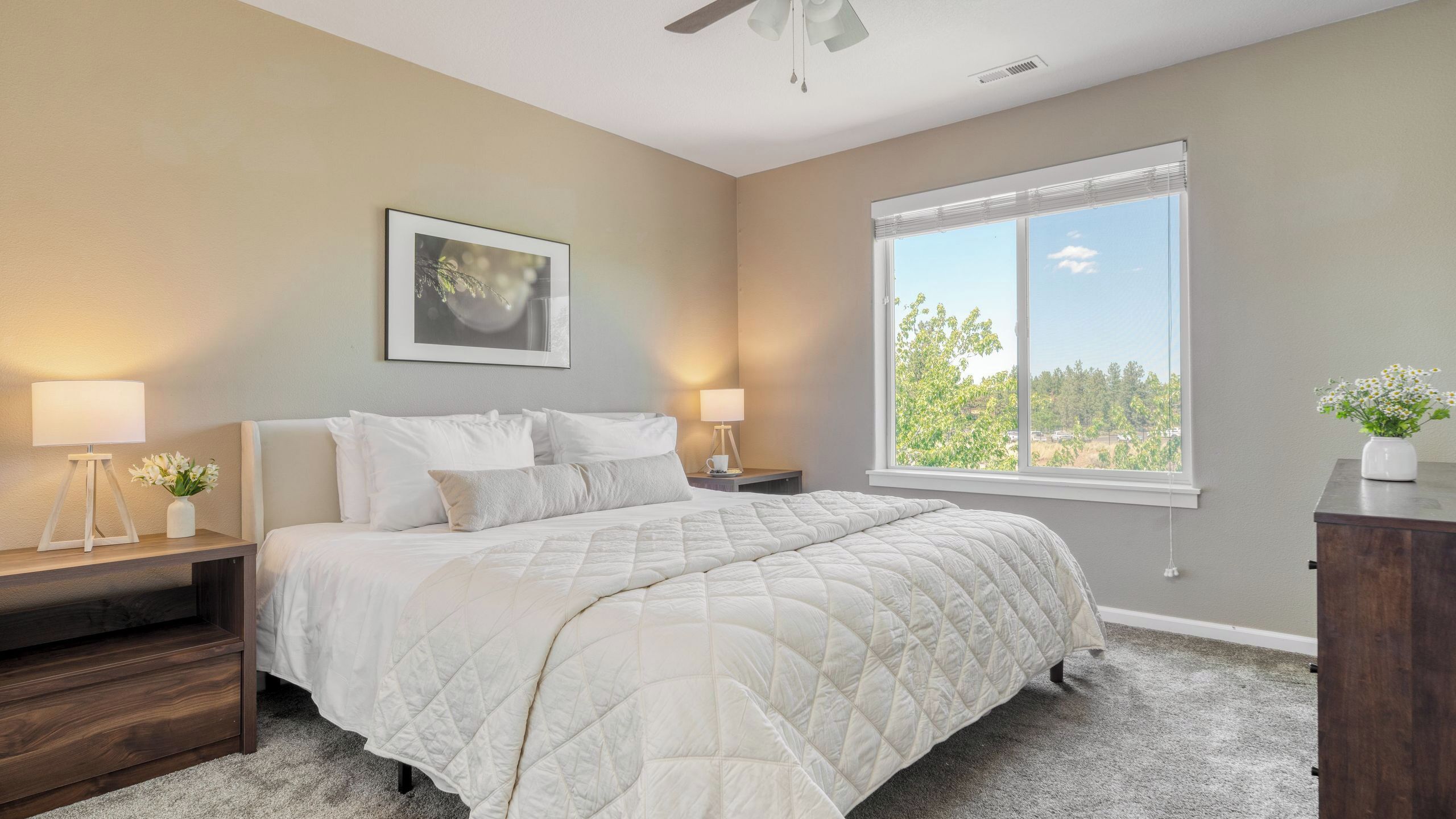 A bedroom with a bed, bedside tables, a window with a view, and a ceiling fan.
