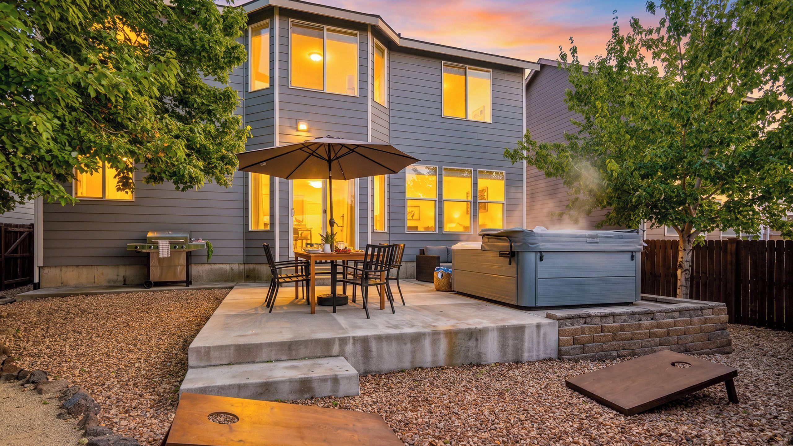 A residential backyard with a patio, outdoor seating, a grill, and a hot tub.