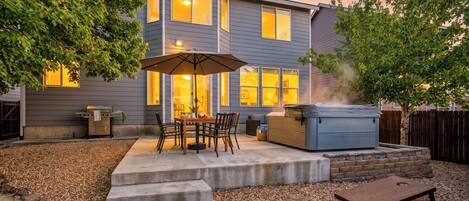 A residential backyard with a patio, outdoor seating, a grill, and a hot tub.