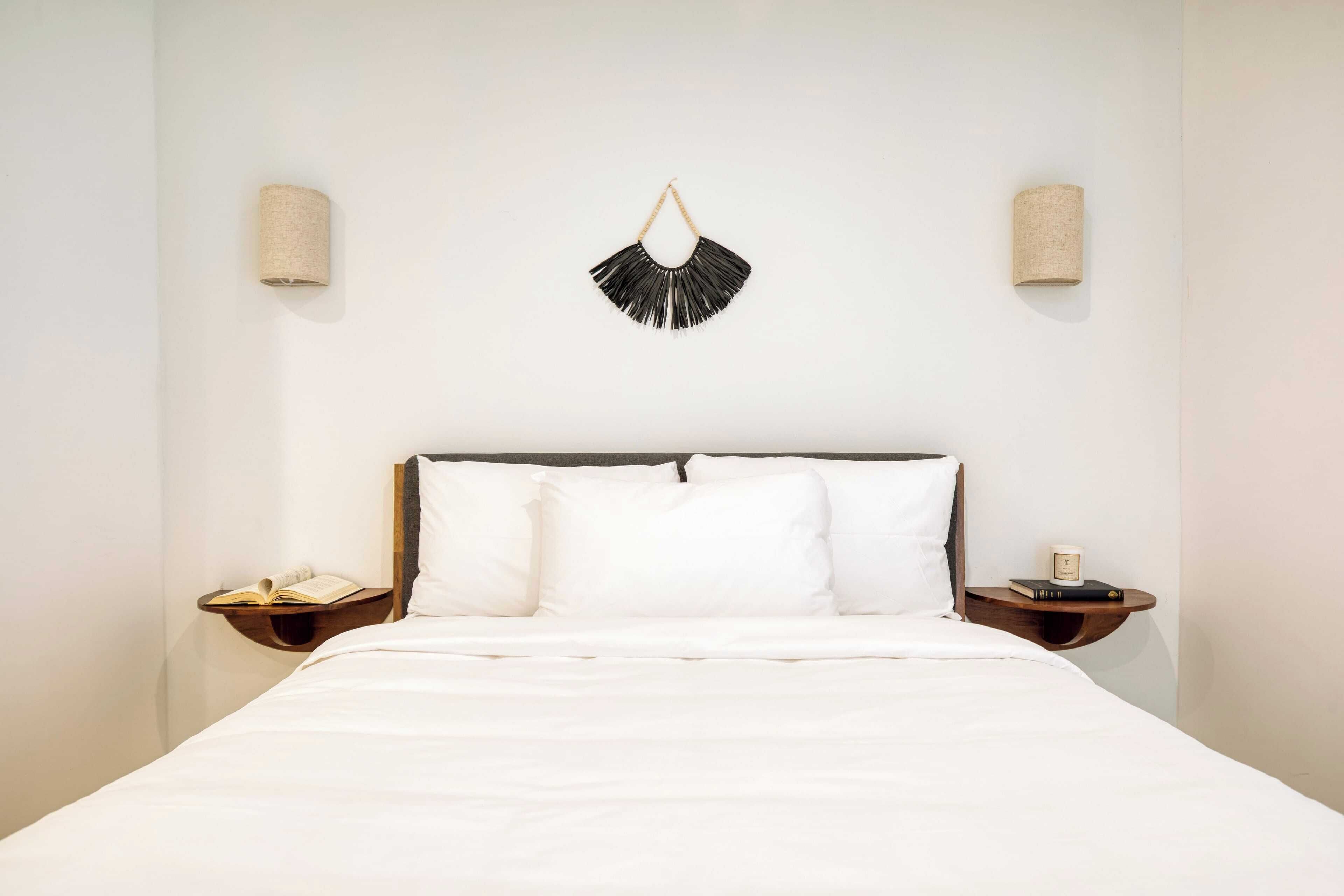 A neatly made bed with white linens, two bedside tables with books and a candle, and a wall-mounted decorative piece above the bed.