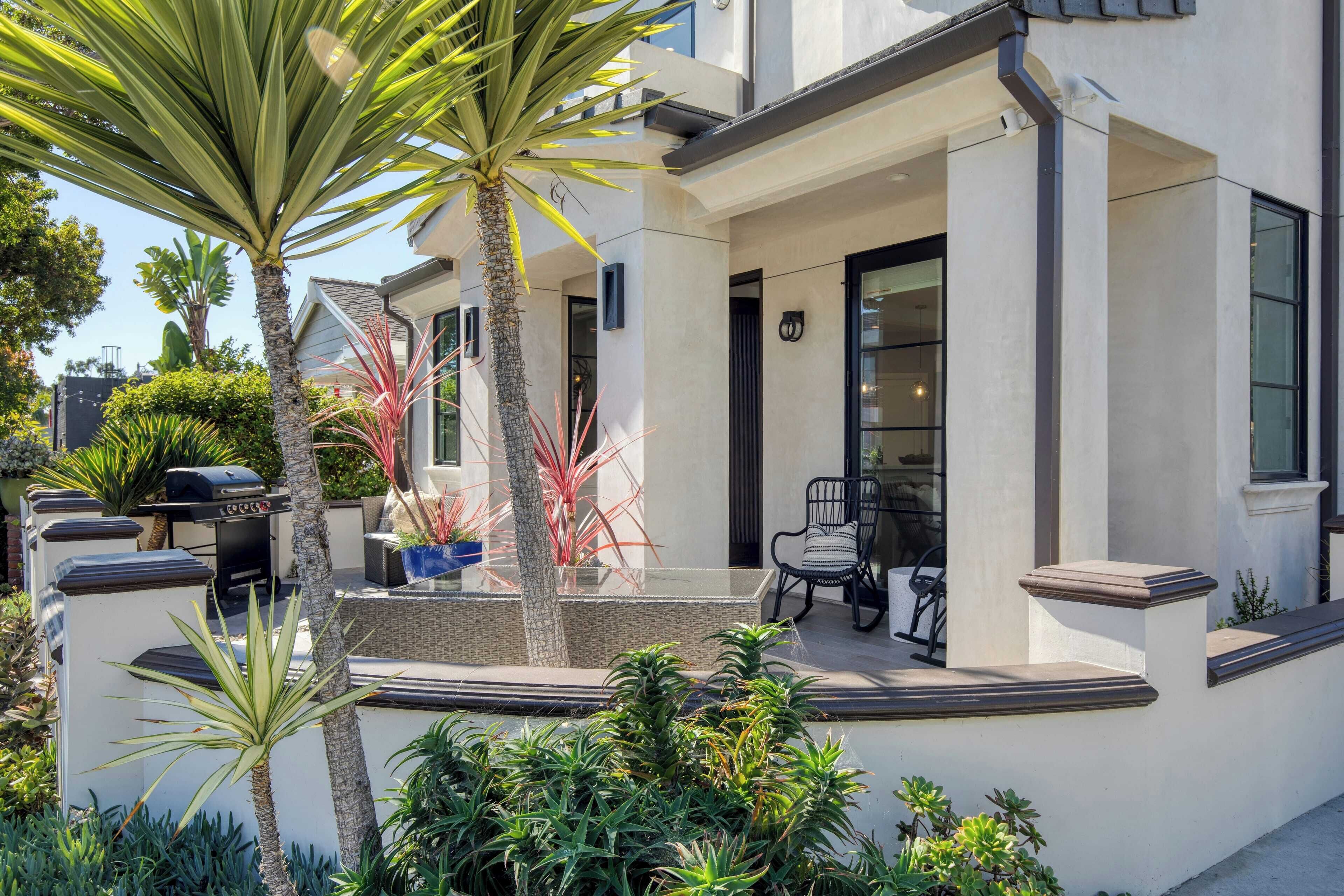 A modern house with a patio, outdoor seating, and a variety of plants.