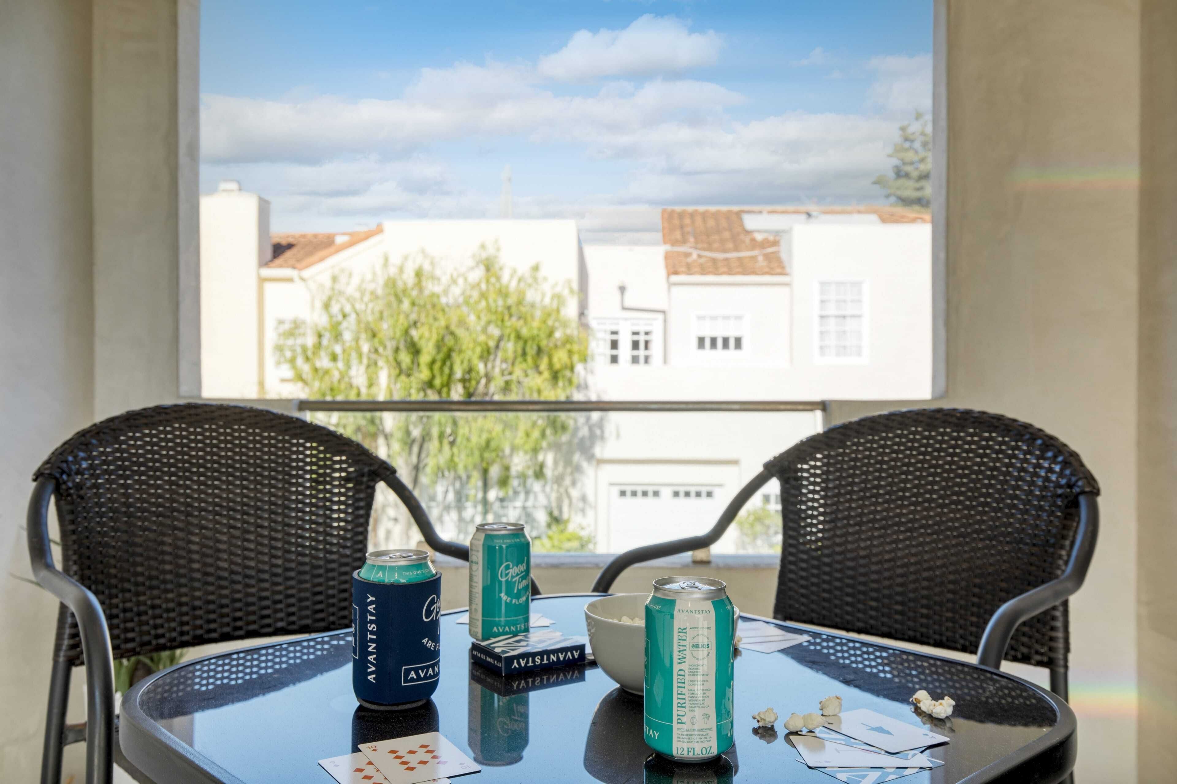Une table avec deux chaises, une fenêtre donnant sur des immeubles et des bouteilles d’eau sur la table.