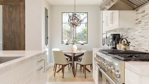 Une cuisine moderne avec une table à manger, des chaises, une cuisinière et un luminaire suspendu.