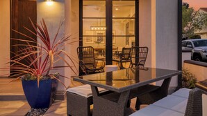An outdoor dining area with a glass table and wicker chairs, a potted plant, and a view of the interior through a glass door. - Sea Crown by Avantstay 5mins From the Beach w/ Multiple Terraces! Permit#slp13639 (Newport Beach)