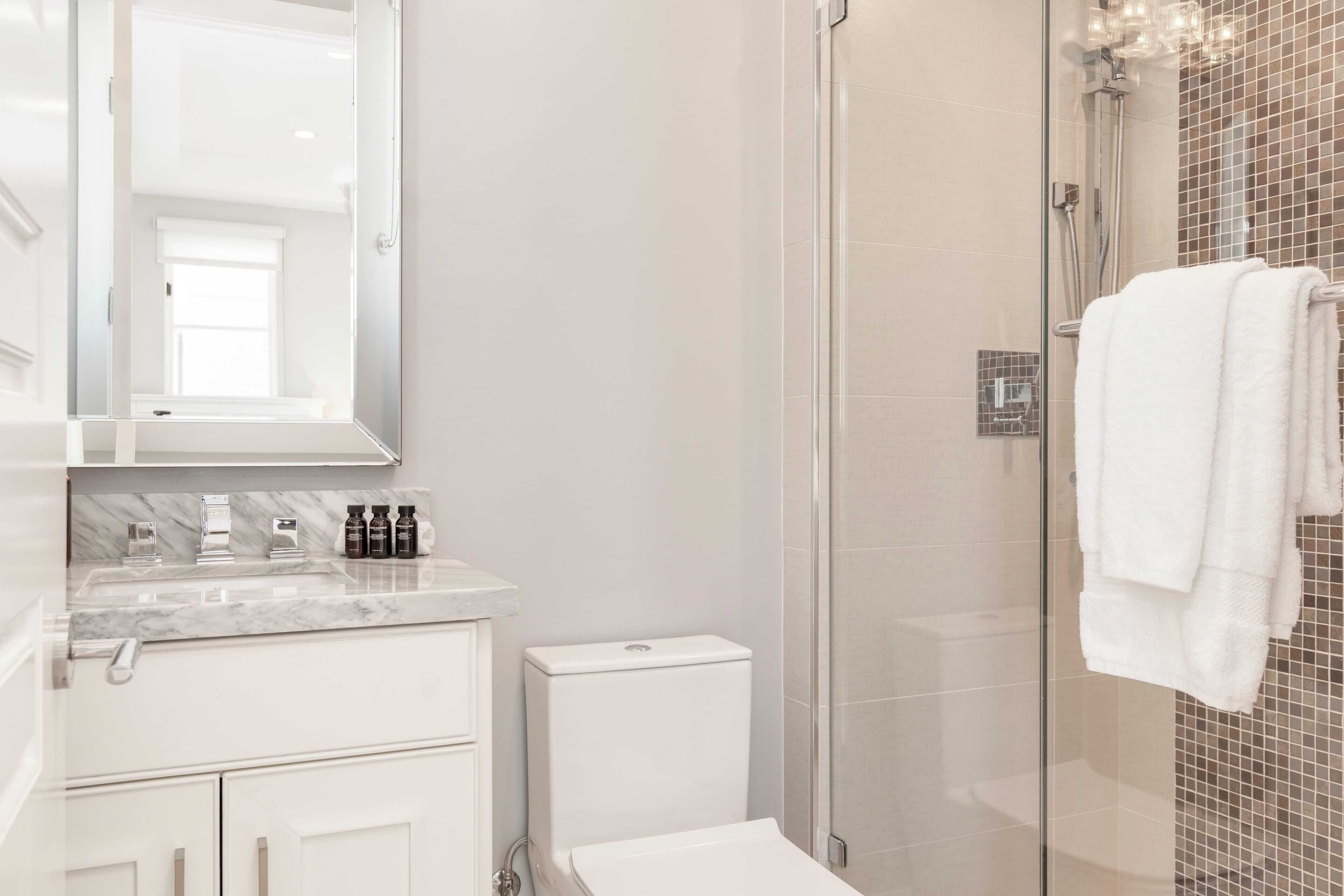 A modern bathroom with a glass shower enclosure, a white toilet, and a marble sink.