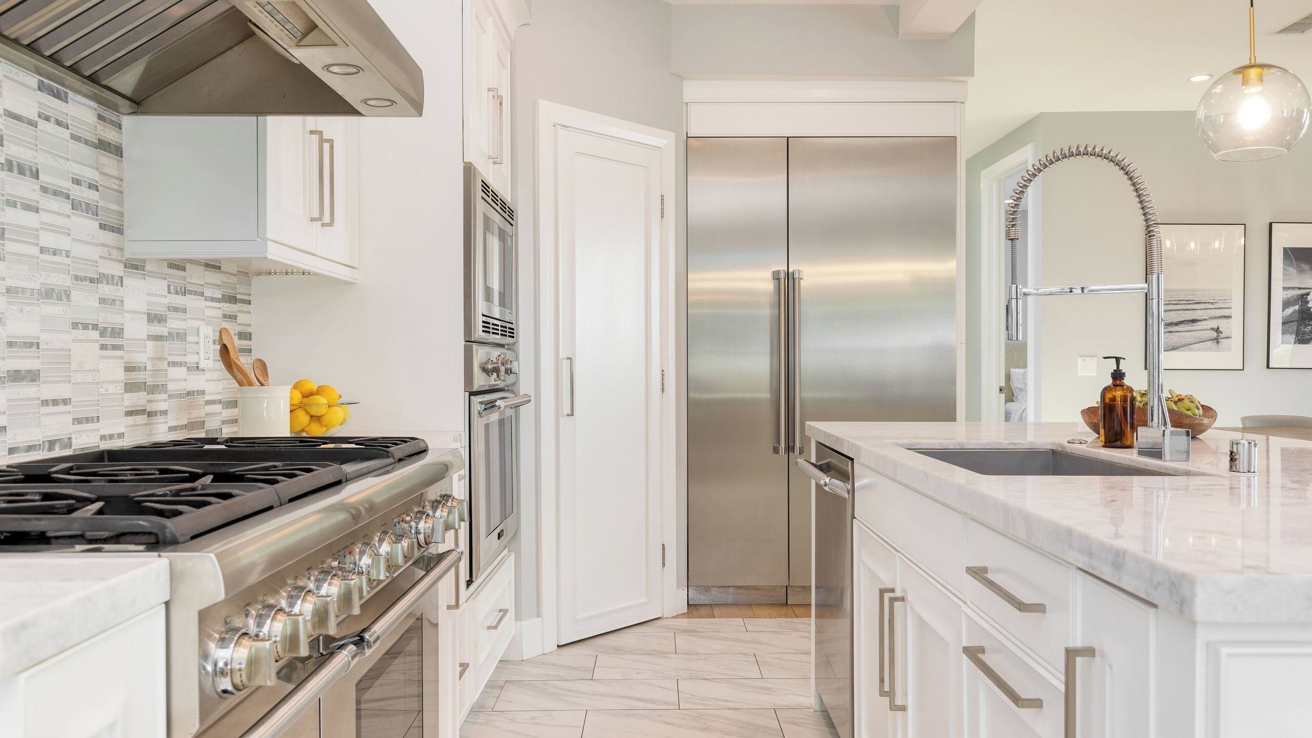 A modern kitchen with a stainless steel refrigerator, a gas stove, and a marble countertop.