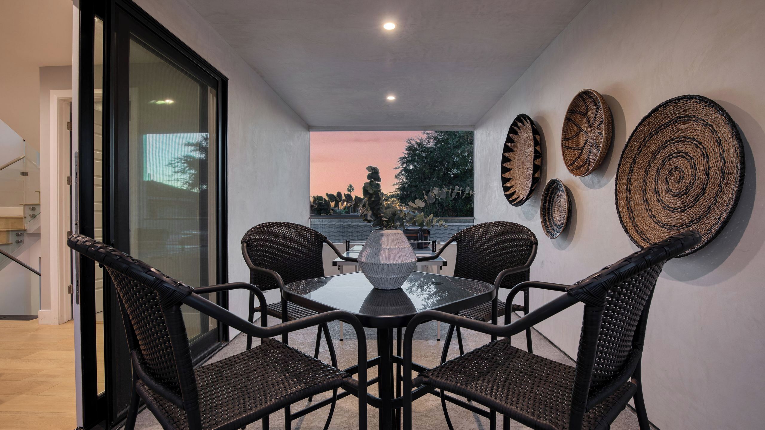 Un patio moderno con una mesa de vidrio y sillas de mimbre, rodeado de cestas tejidas decorativas.