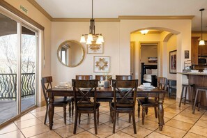 Un espace repas comprenant une grande table, des chaises et un lustre. Une porte-fenêtre coulissante donne accès à un balcon.