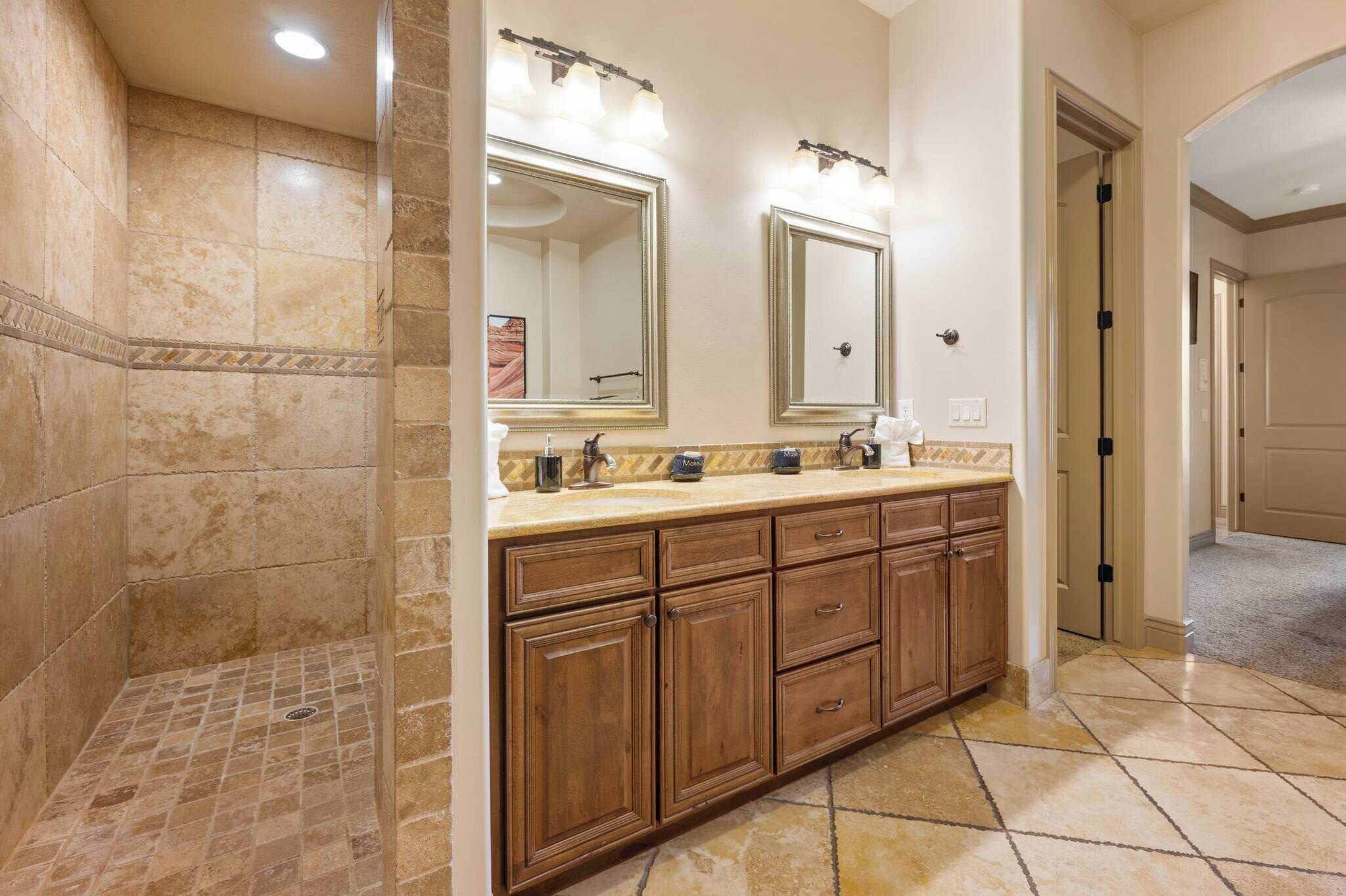 A bathroom with a walk-in shower, double vanity with a large mirror, and a tiled floor.