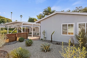 Une maison moderne dotée d’un patio couvert, d’un petit jardin avec des cactus et d’une façade blanche.