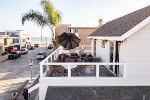 A balcony with outdoor seating, overlooking a street with parked cars and a beach in the background. - Sea Sight by Avantstay Walk to Newport Beach (Newport Beach)