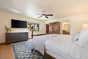 Une chambre à coucher comprenant un lit, un ventilateur de plafond, une télévision, une commode et une fenêtre donnant sur un paysage verdoyant.