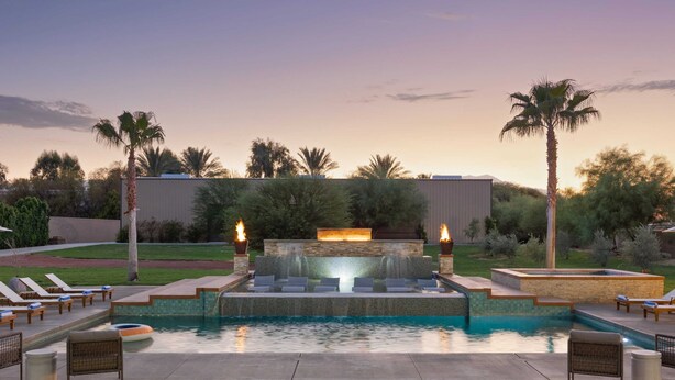 A pool area with lounge chairs, a water feature, and a stone wall.