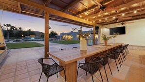 An outdoor patio with a wooden table and chairs, ceiling fans, and string lights.