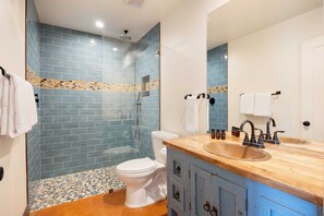 Une salle de bain avec des murs recouverts de carreaux bleus, des toilettes blanches, une douche en verre et un meuble-lavabo en bois avec un évier.