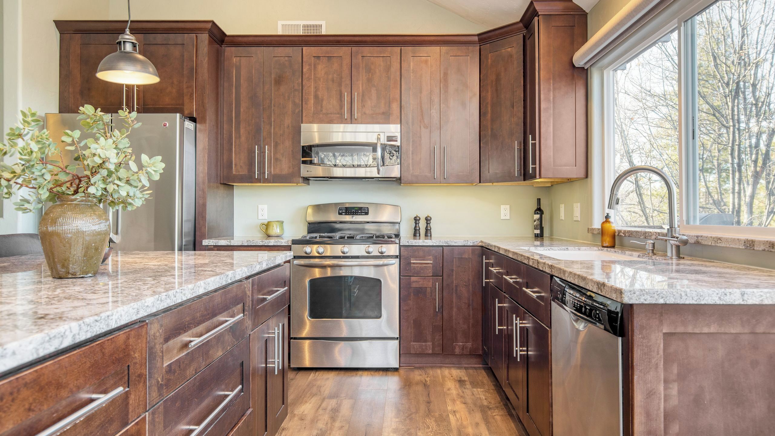Una cocina moderna con armarios de madera oscura, electrodomésticos de acero inoxidable y un amplio ventanal con vistas a árboles.