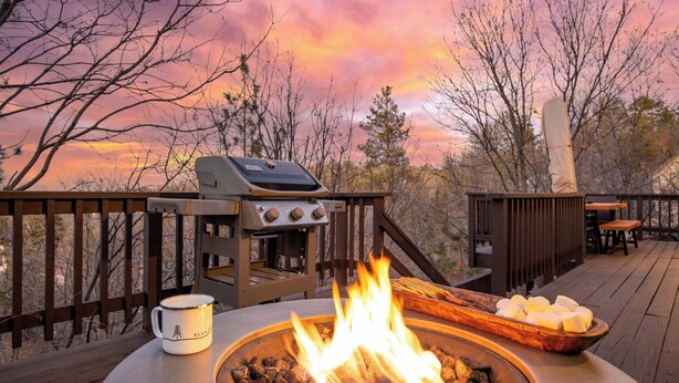 An outdoor barbecue area with a grill, a fire pit, and a table with a mug.