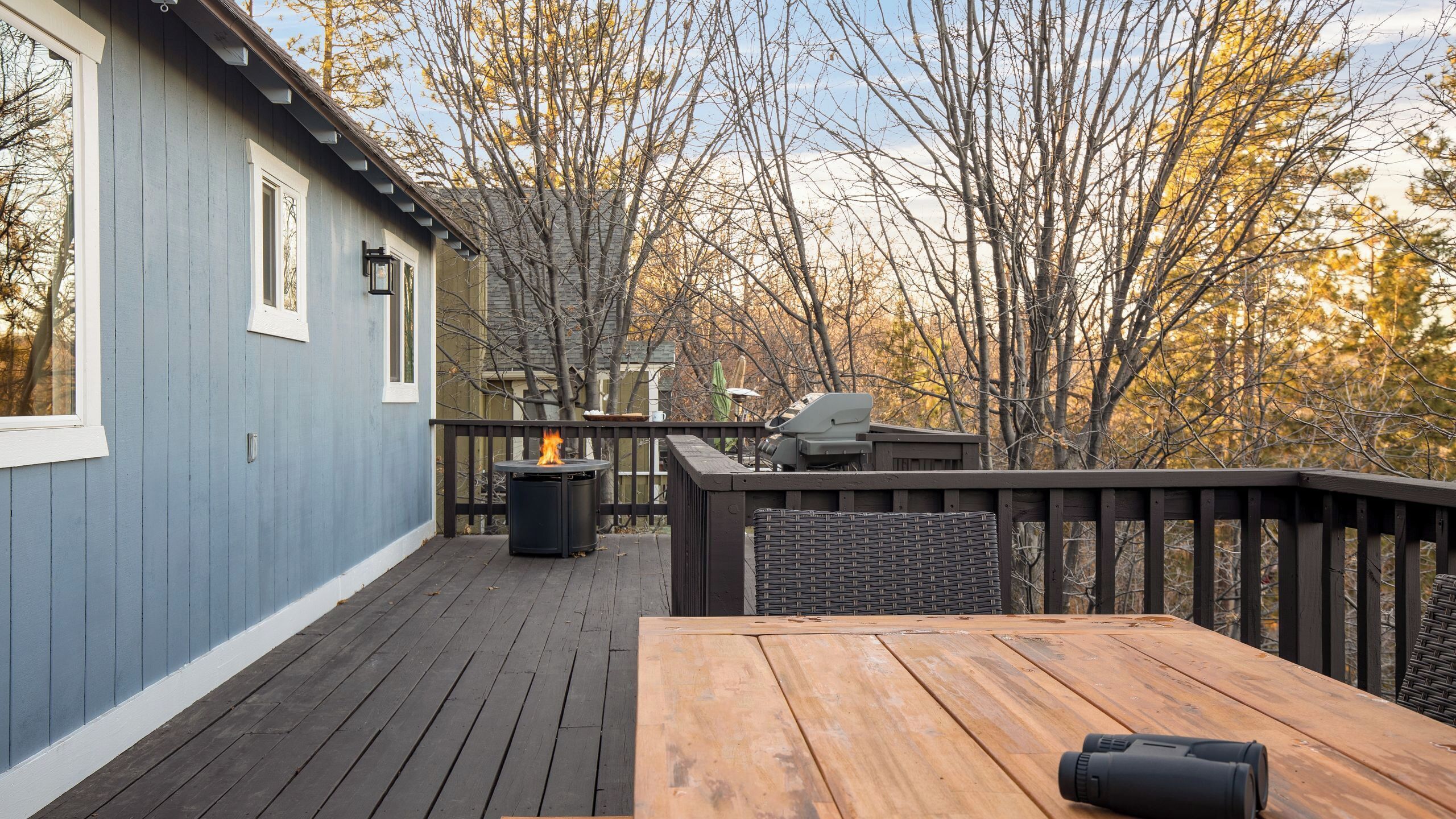 Une terrasse en bois avec une table et des chaises, un barbecue et un foyer.