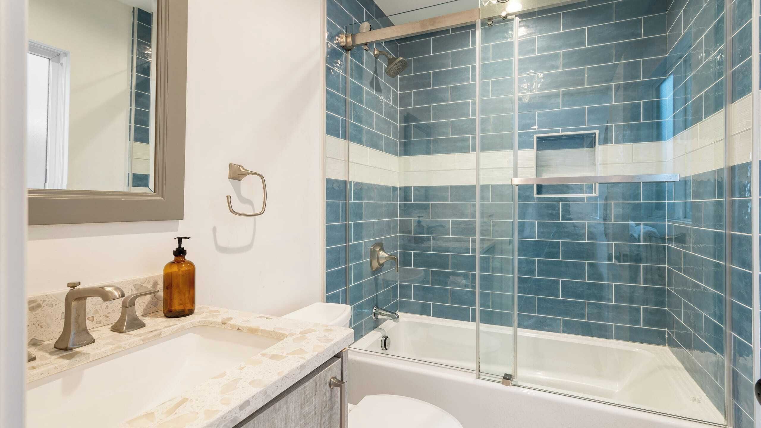 Un baño con ducha envuelta en vidrio, una bañera blanca y encimera de mármol con dispensador de jabón.