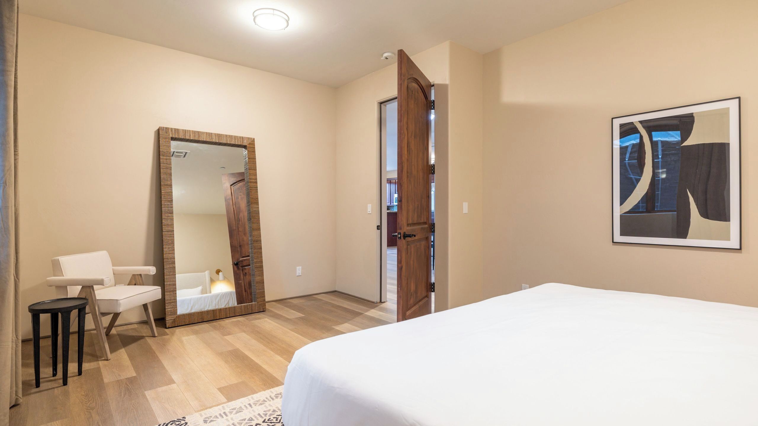 Un dormitorio con cama, un espejo grande, una puerta y un cuadro enmarcado en la pared.