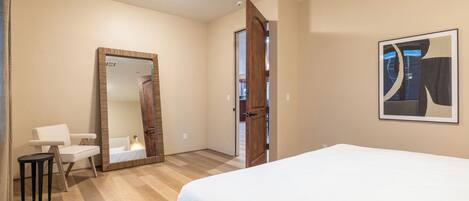 Un dormitorio con cama, un espejo grande, una puerta y un cuadro enmarcado en la pared.
