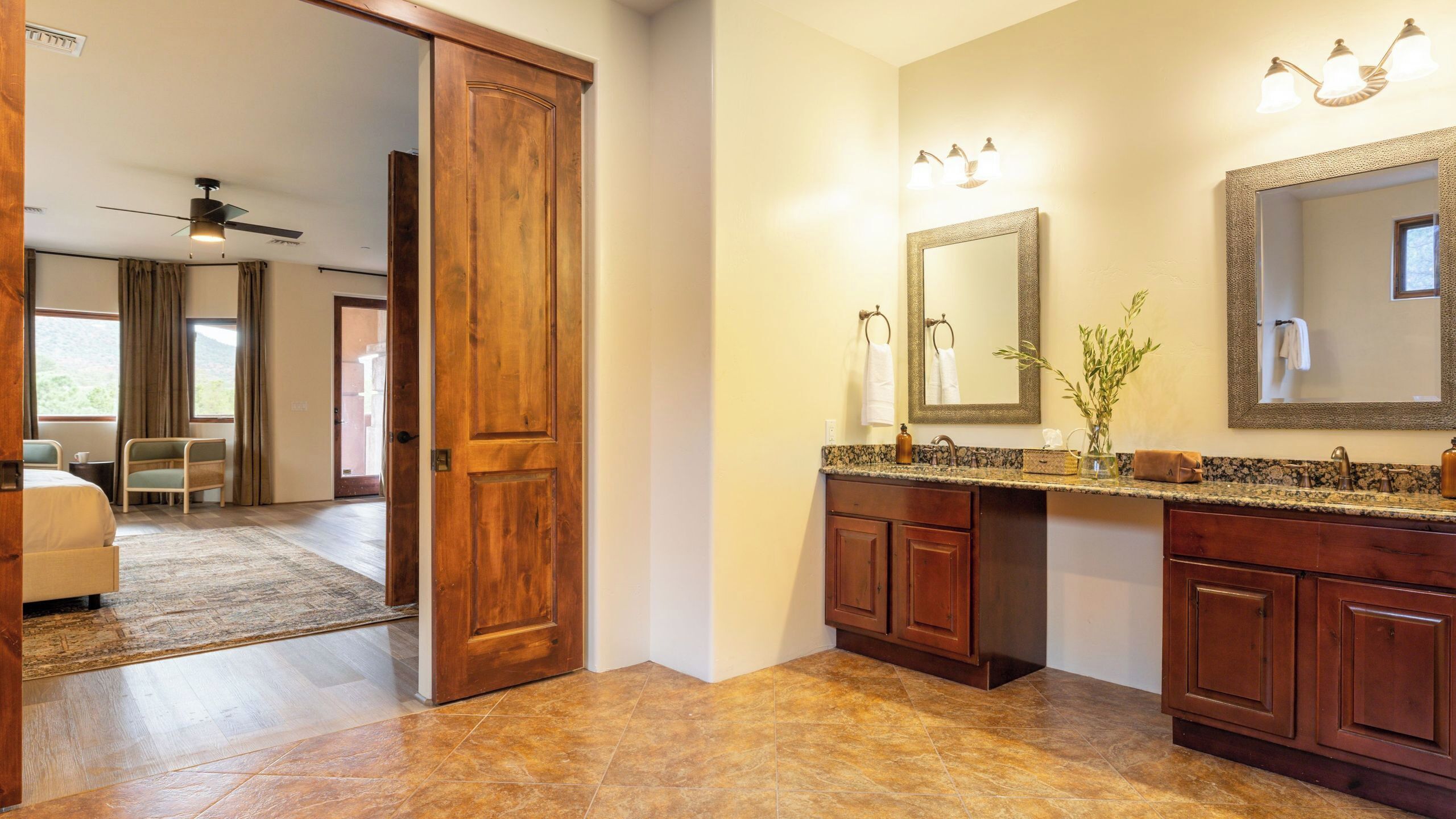 A bathroom with a double sink, wooden cabinets, a large mirror, and a ceiling fan.
