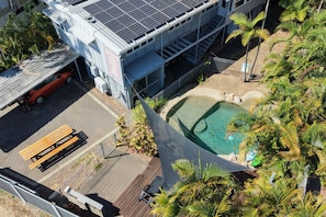 Een gebouw met zonnepanelen, een zwembad en een parkeerplaats met een bankje.