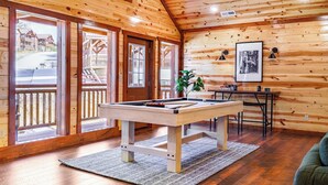 A wooden interior with a pool table, a framed picture, and a view of the outside deck.