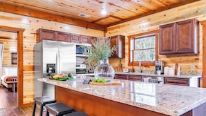A kitchen with wooden walls, a granite countertop, and a large island with stools.