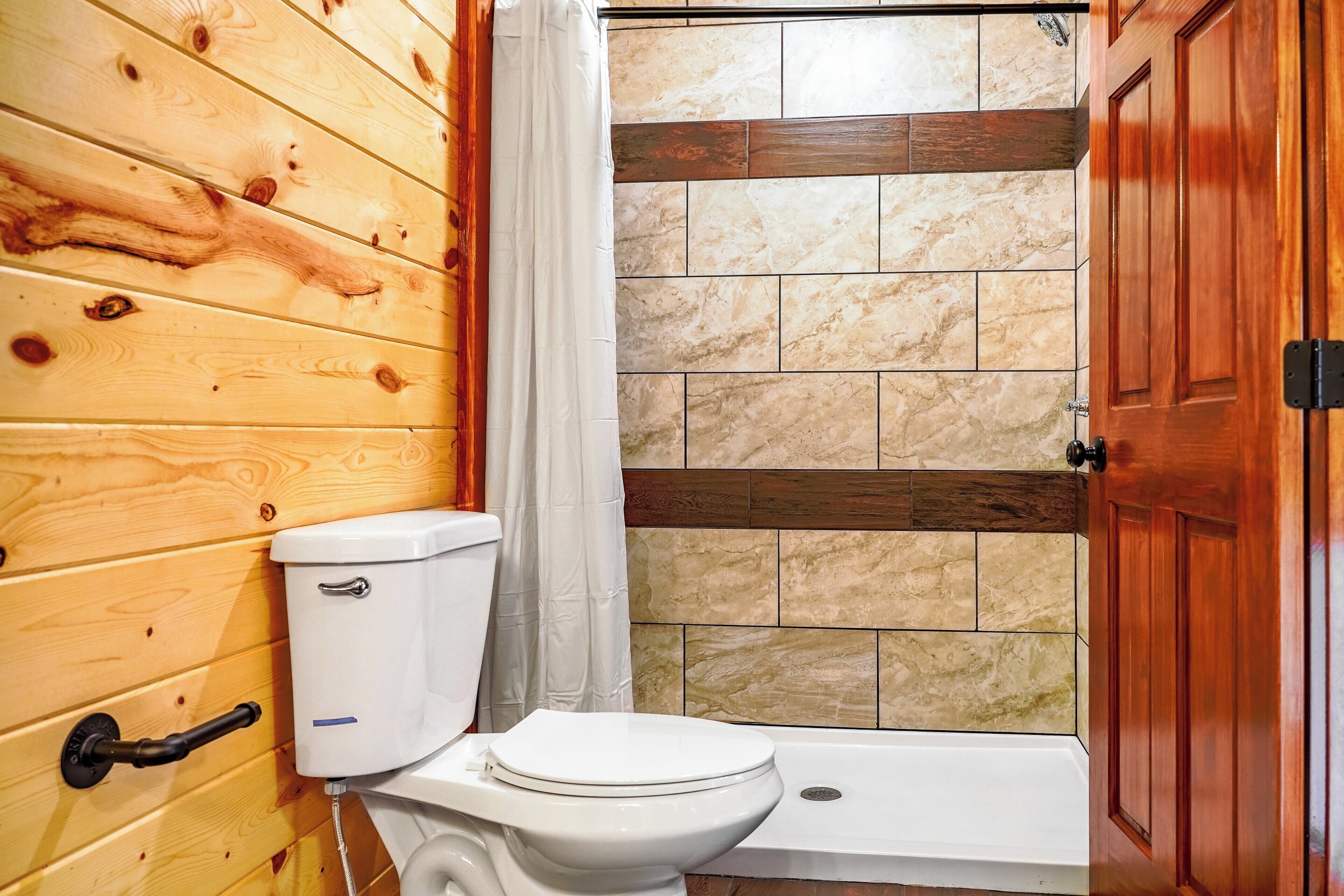 A wooden-paneled bathroom with a white toilet, a shower area with tiled walls, and a wooden door.