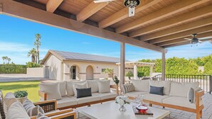 An outdoor patio area with a covered seating area, a table with a vase of flowers, and a view of a house with solar panels. - Pool, Sports Court, Game Garage, & Fire Pit Olivano Ranch by Avantstay (Palm Desert)