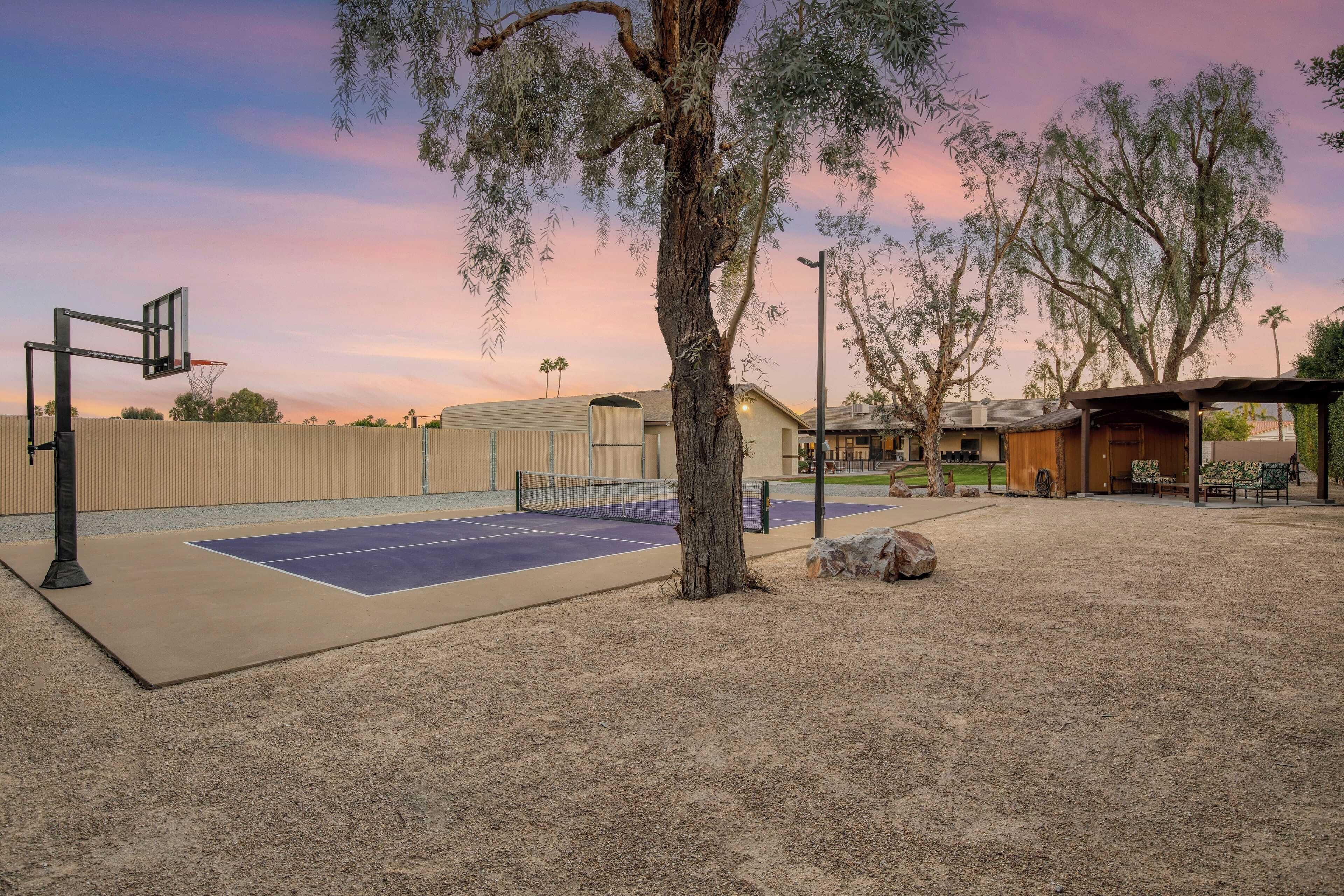 An outdoor basketball court with a net, surrounded by trees and a building in the background.
