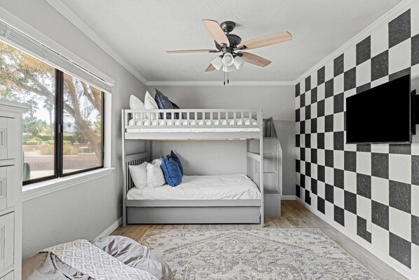 A room with a bunk bed, a ceiling fan, a large window, and a checkered wall.