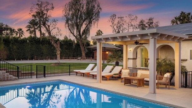 A pool area with lounge chairs and a covered seating area, surrounded by trees and a clear sky. - Pool, Sports Court, Game Garage, & Fire Pit Olivano Ranch by Avantstay (Palm Desert)