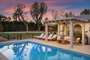 A pool area with lounge chairs and a covered seating area, surrounded by trees and a clear sky. - Pool, Sports Court, Game Garage, & Fire Pit Olivano Ranch by Avantstay (Palm Desert)