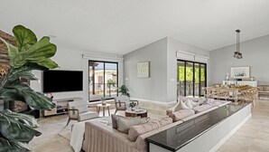 A spacious living area with a large sofa, a flat-screen TV, and a dining area with a table and chairs. - Pool, Sports Court, Game Garage, & Fire Pit Olivano Ranch by Avantstay (Palm Desert)