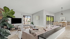 A spacious living area with a large sofa, a flat-screen TV, and a dining area with a table and chairs.