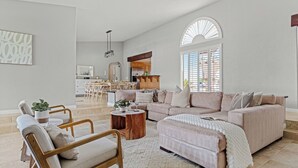 A spacious living room with a large sofa, a coffee table, and a dining area with a kitchen in the background. - Pool, Sports Court, Game Garage, & Fire Pit Olivano Ranch by Avantstay (Palm Desert)