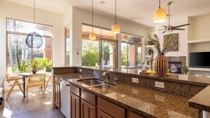 A modern kitchen with granite countertops, a stainless steel sink, and pendant lighting.