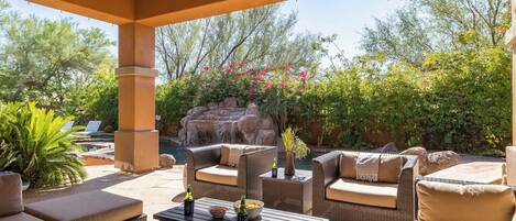 An outdoor patio with wicker furniture, a small waterfall feature, and lush greenery.