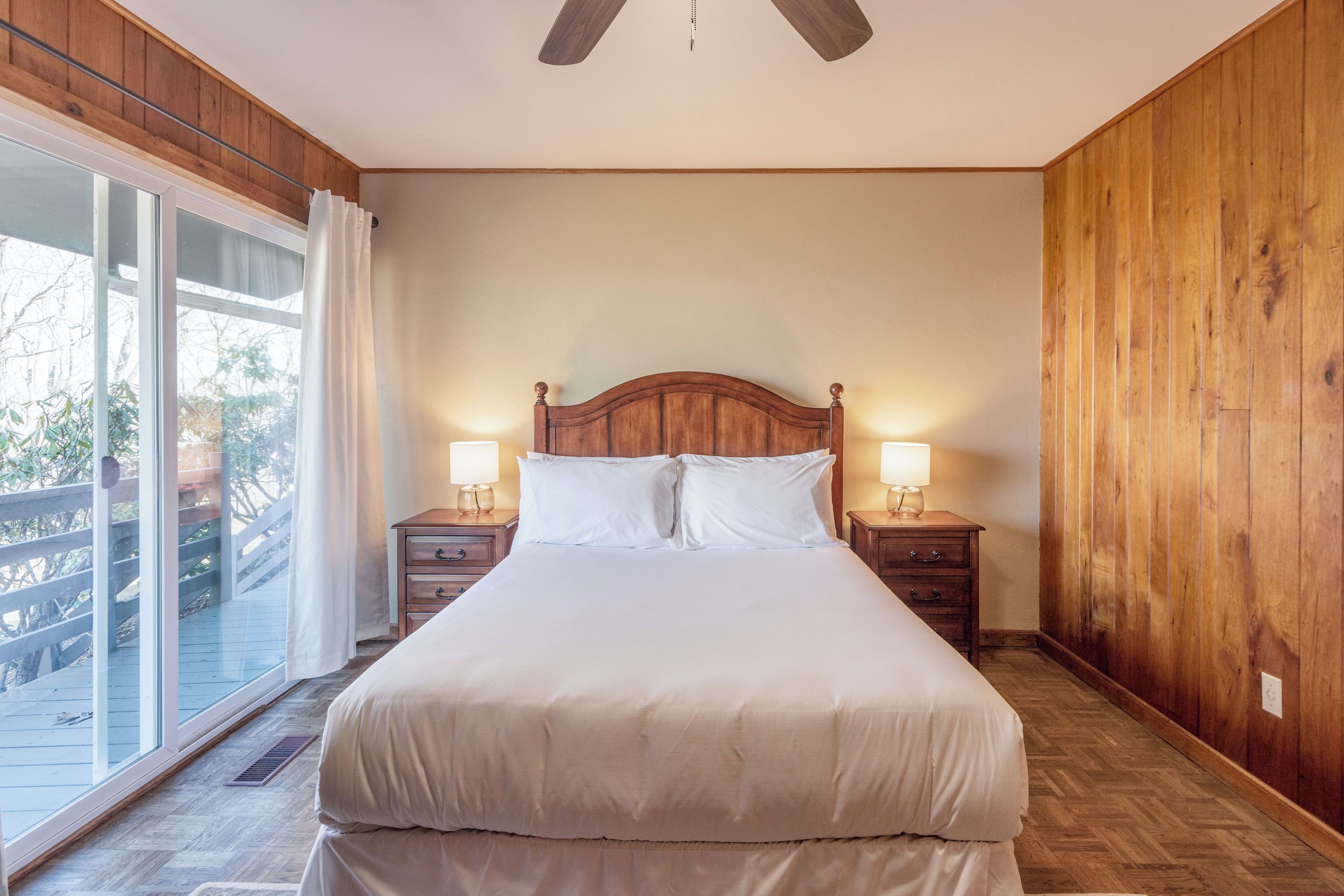 Een slaapkamer met een groot bed, houten wanden, een plafondventilator en uitzicht door een schuifdeur op een terras.