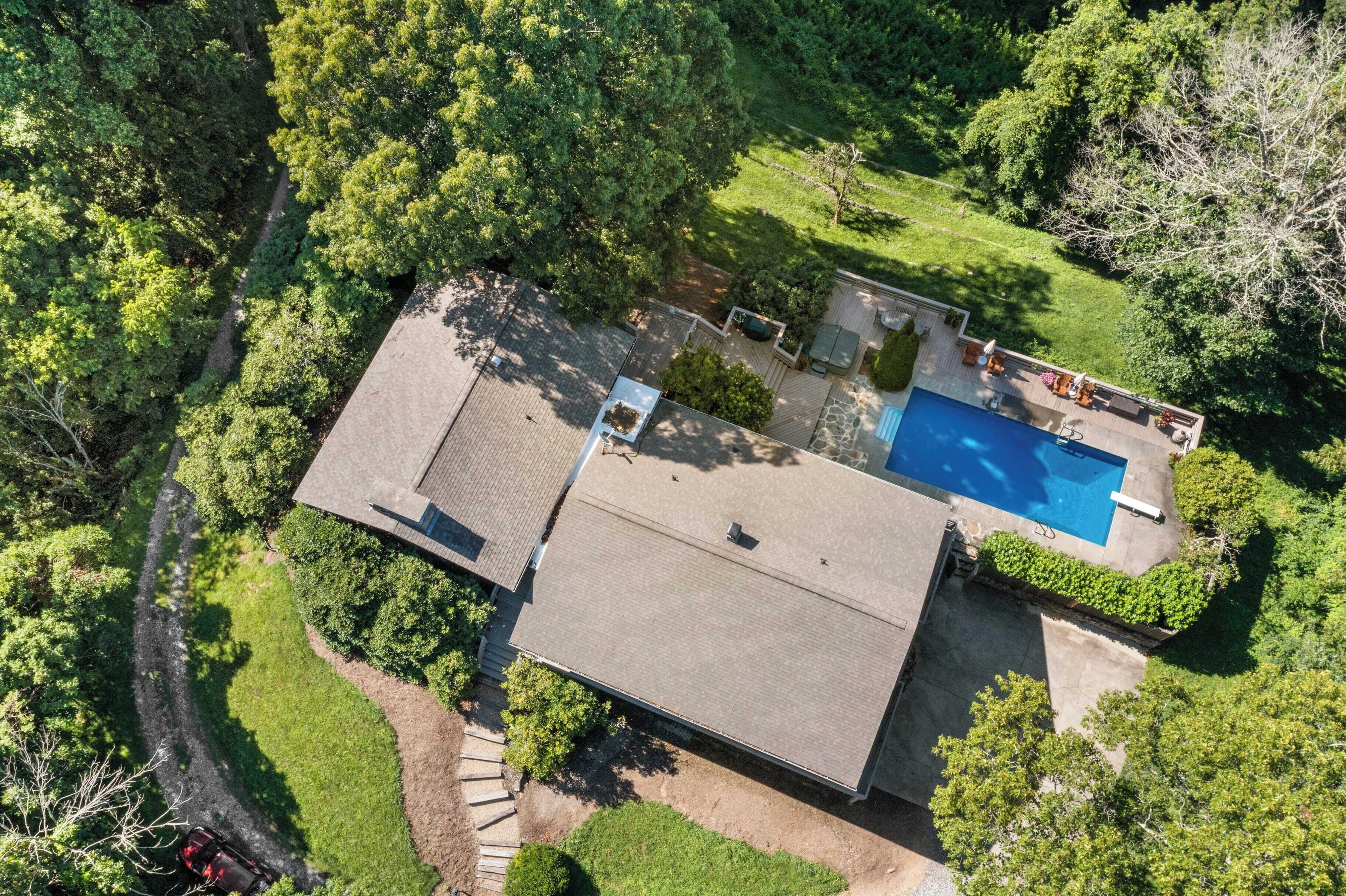 An aerial view of a house with a swimming pool, surrounded by lush greenery.