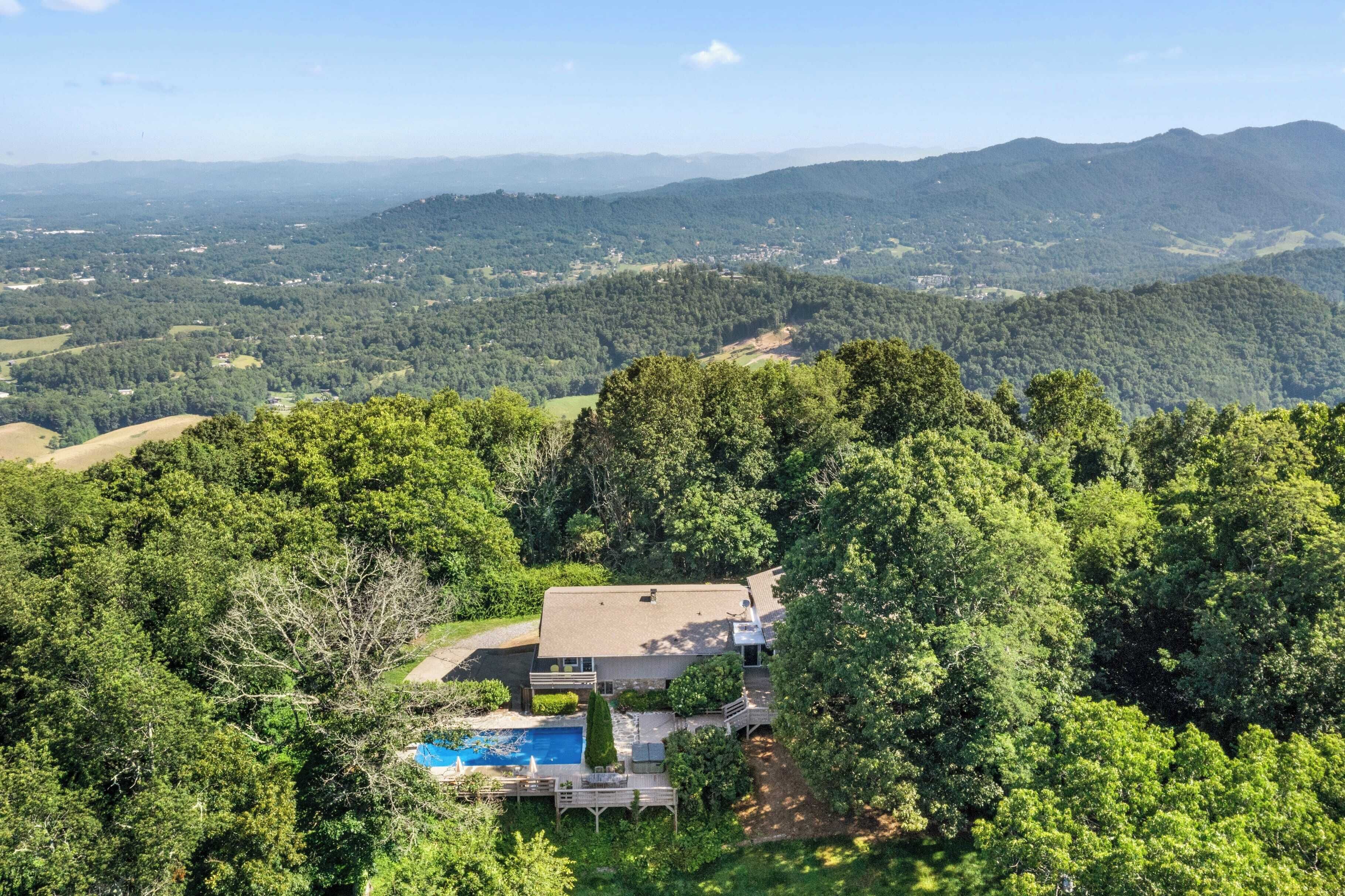 A large house surrounded by dense forest, with a swimming pool and a deck.