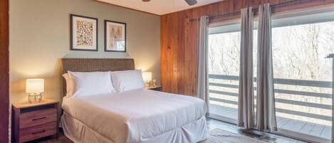 A bedroom with a large bed, wooden walls, a ceiling fan, and a window with curtains.