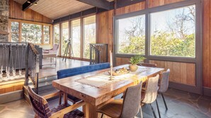 A spacious dining area with a wooden table, chairs, and a large window offering a view of trees. - Asher by Avantstay Mountain Escape + Pool/spa (Weaverville)