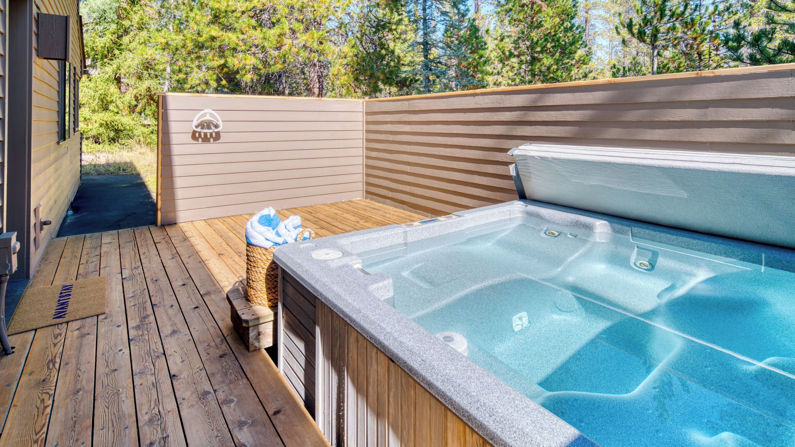Une terrasse en bois avec un jacuzzi, une serviette et un paillasson.