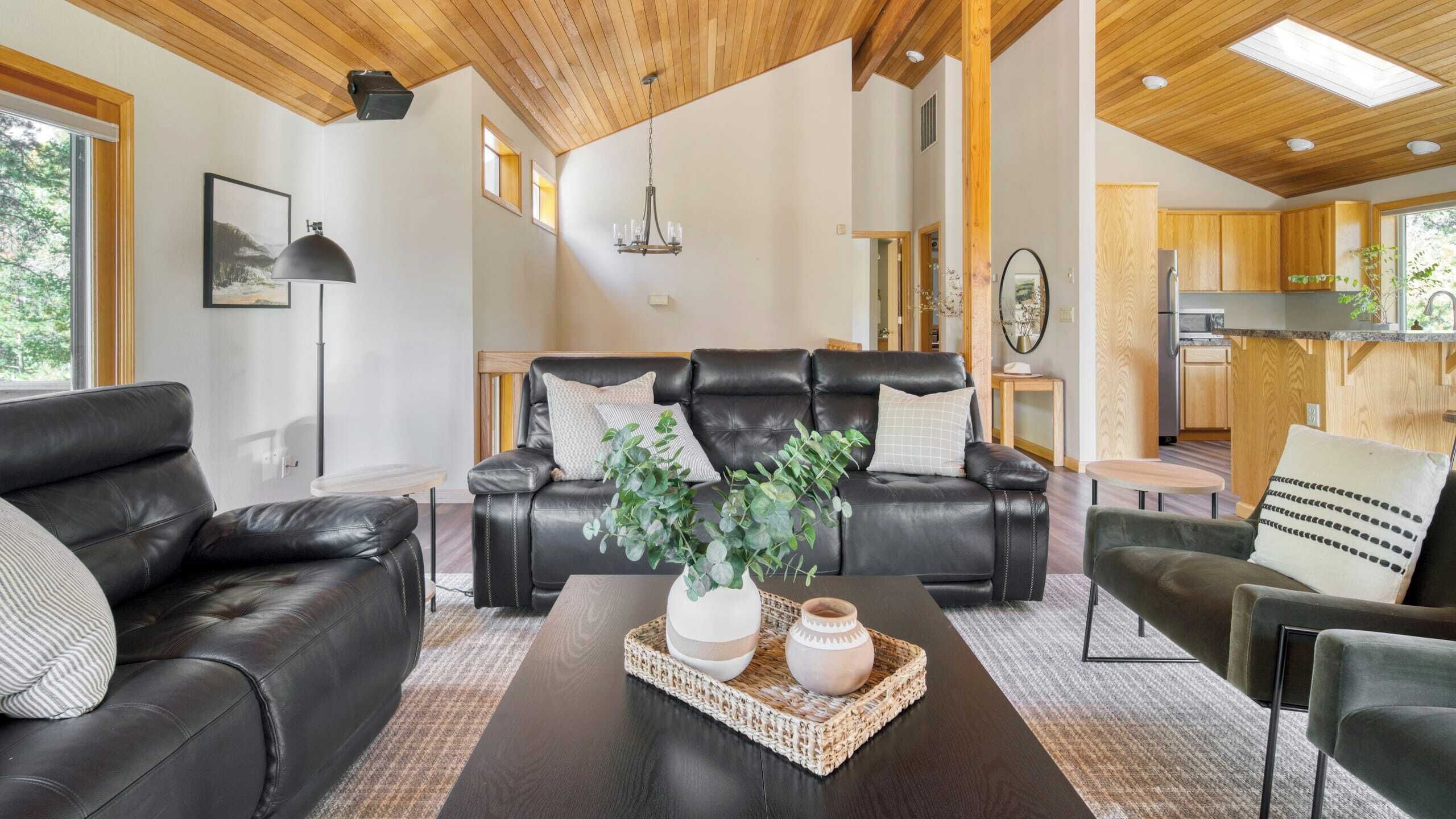 A modern living room with leather sofas, a coffee table with decorative items, and a view into the kitchen area.