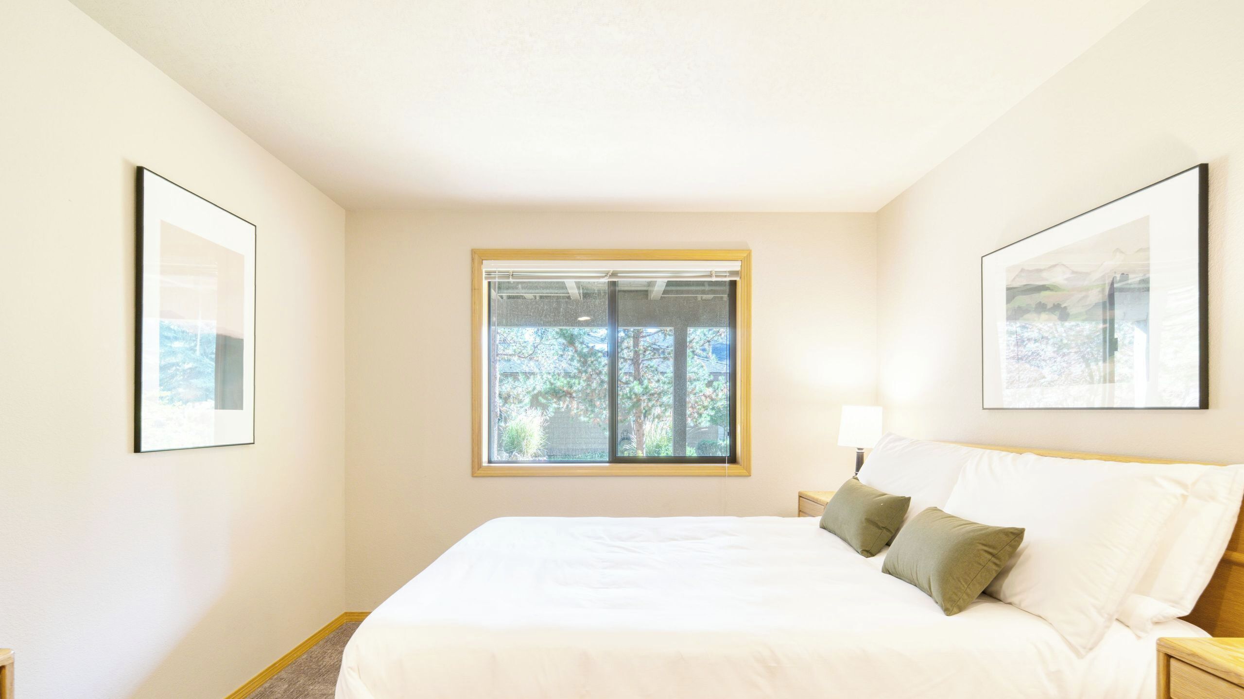 Une chambre à coucher avec un grand lit, une fenêtre donnant sur la verdure et deux tableaux encadrés accrochés aux murs.