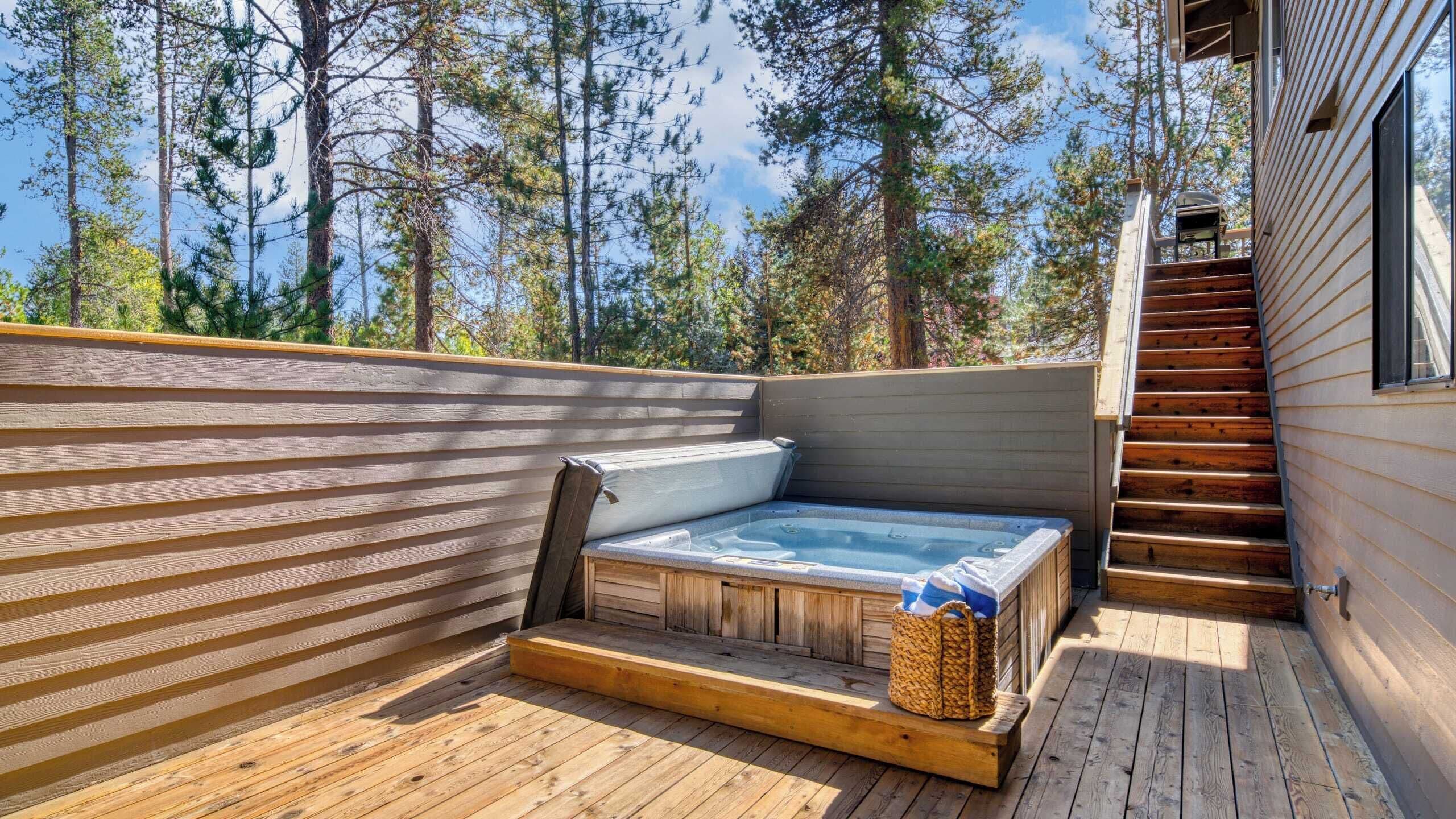 A wooden deck with a hot tub, wooden steps, and a view of trees.