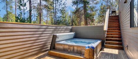 A wooden deck with a hot tub, wooden steps, and a view of trees.